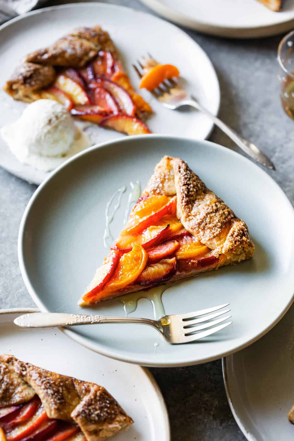 a slice of stone fruit galette sits on a matte blue plate drizzled with golden honey
