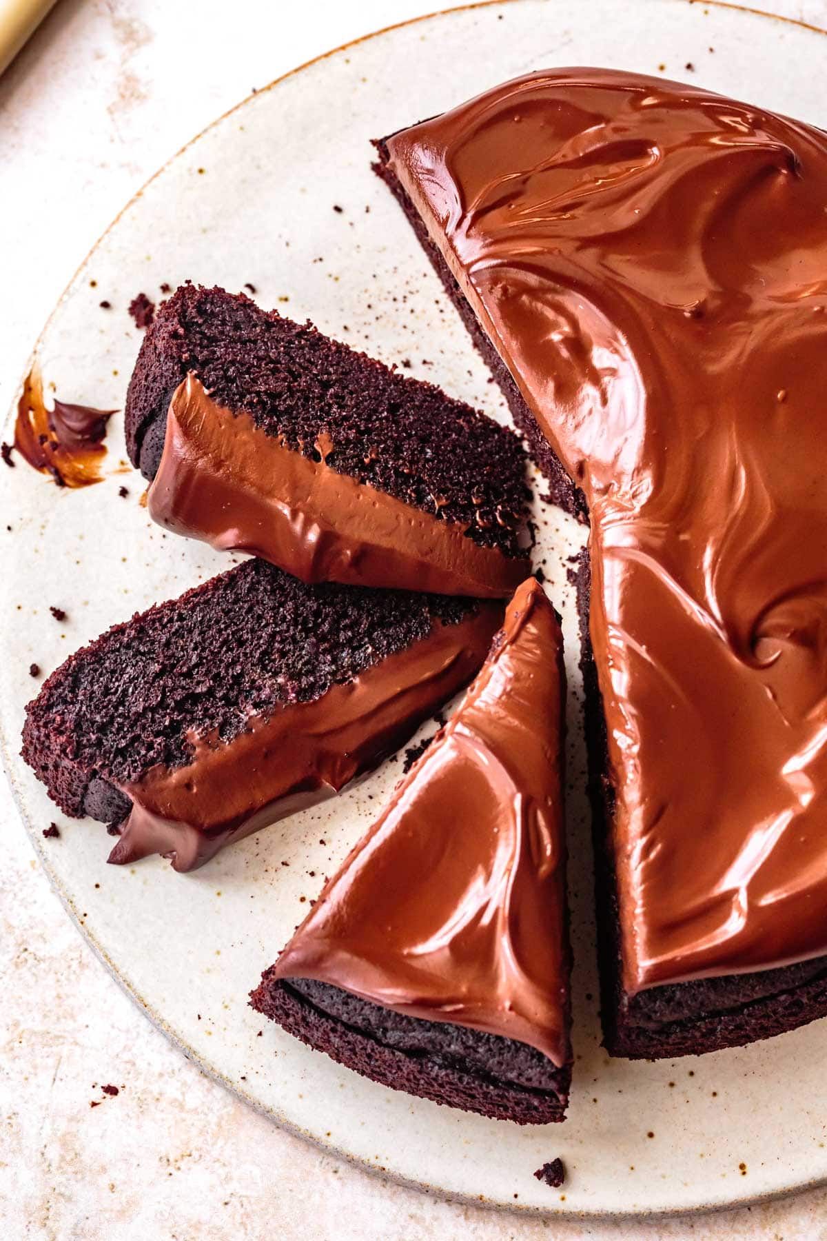 a chocolate cake with a pillowy crumb has been topped with glossy swirls of ganache and sliced