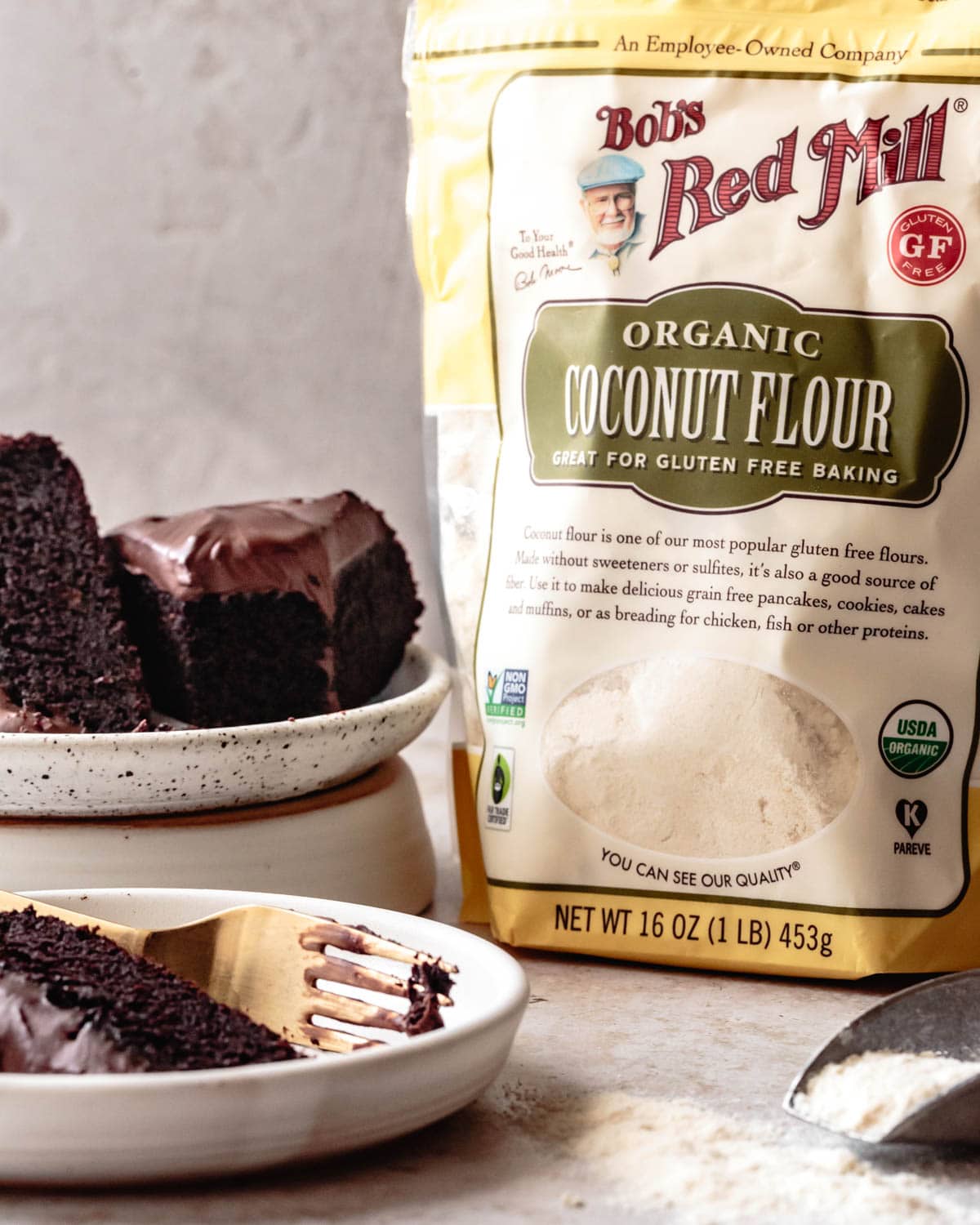 a bag of heroic-looking coconut flour sits alongside plates with slices of gooey, moist chocolate coconut flour cake