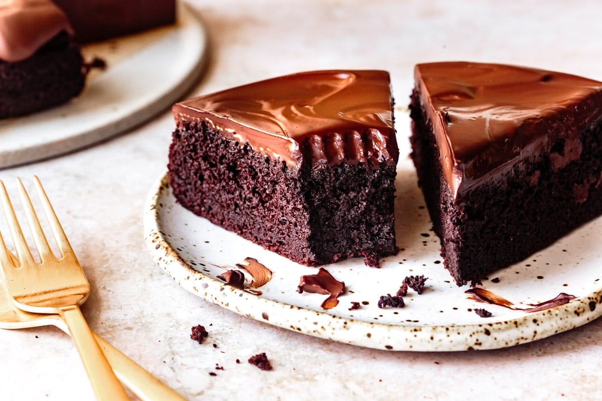 two slices of dark chocolate cake on a cute speckled plate, one slice has a forkful taken out