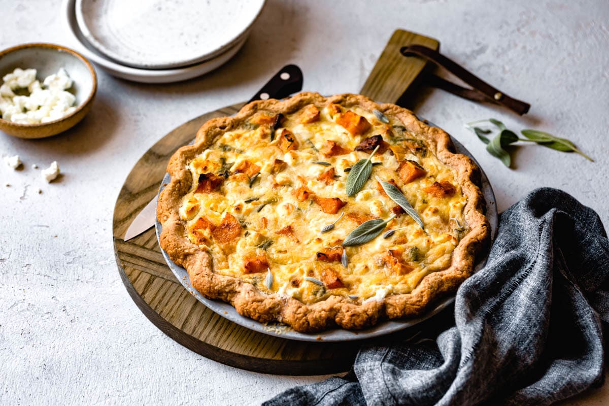 the baked quiche in all its glory. Shown on a round wooden board with a knife laying alongside
