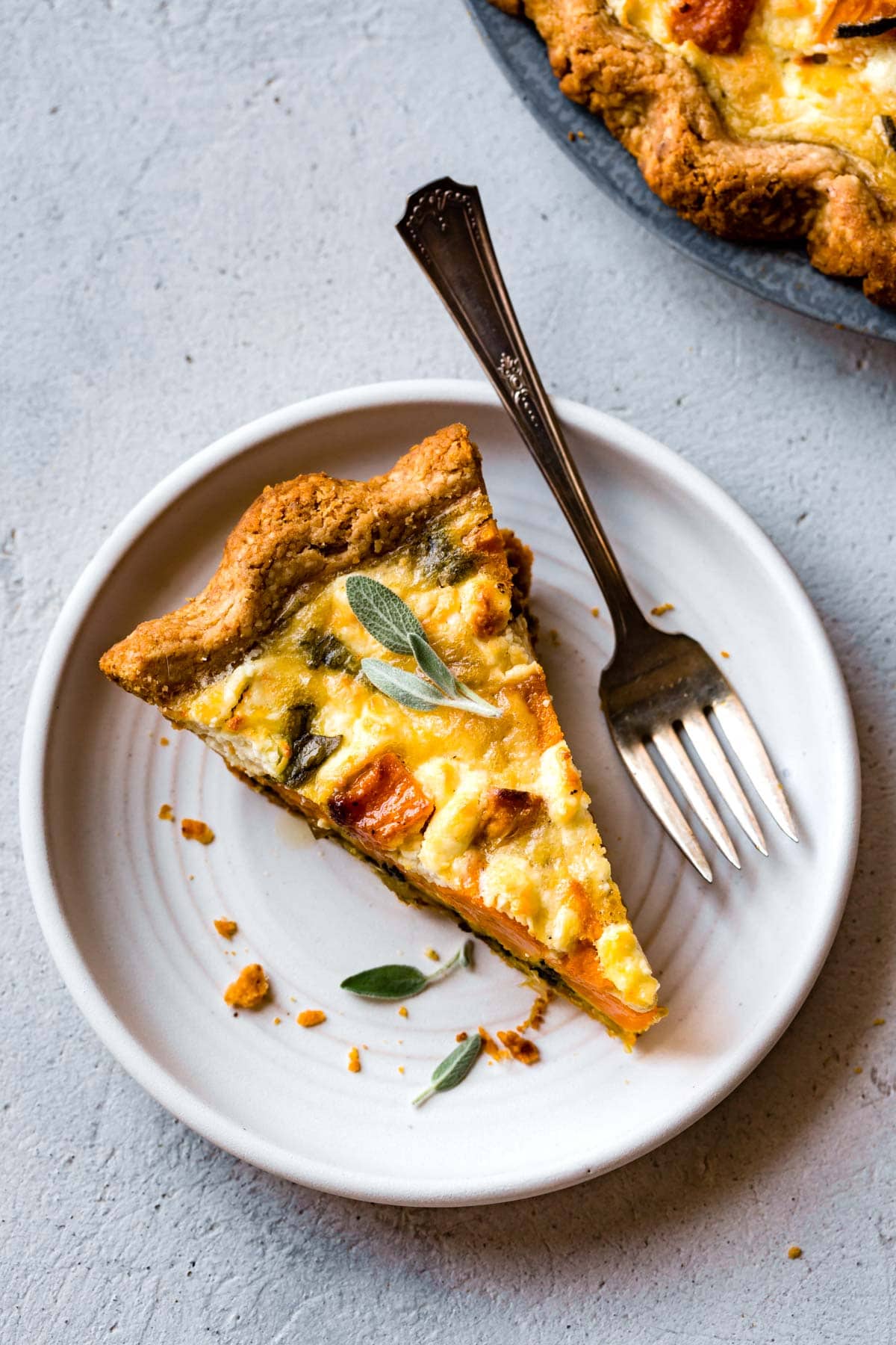 a slice of quiche is on a white plate with a silver vintage fork