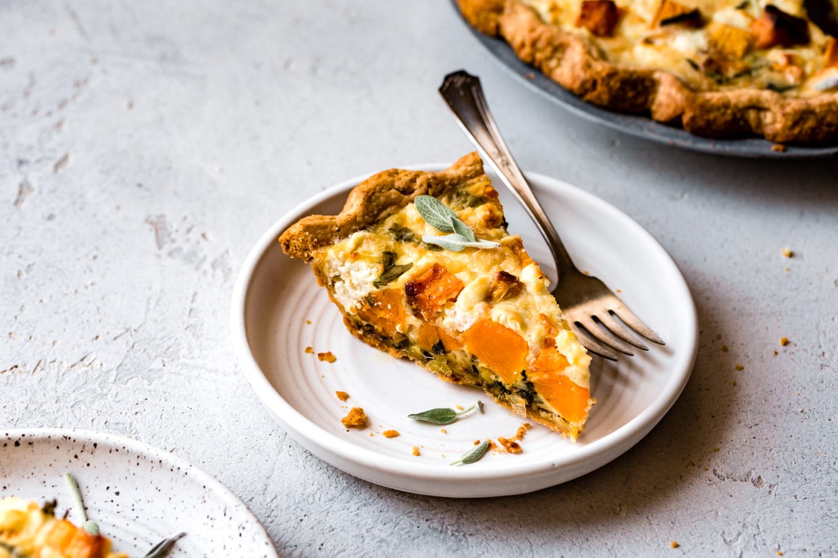 a slice of quiche is shown from the side to reveal a mosaic of bright orange squash cubes