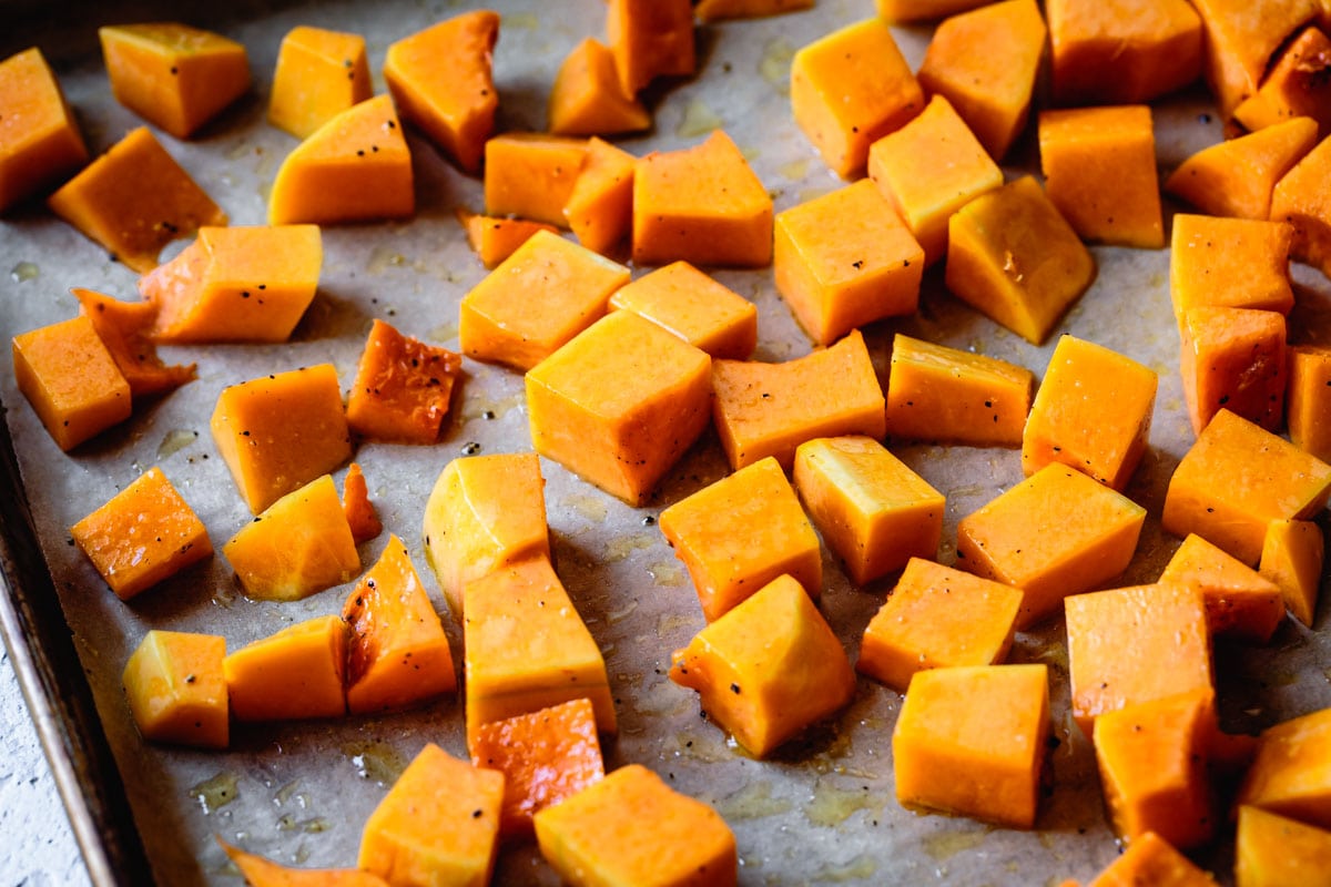 squash cubes are tossed with oil on a baking sheet
