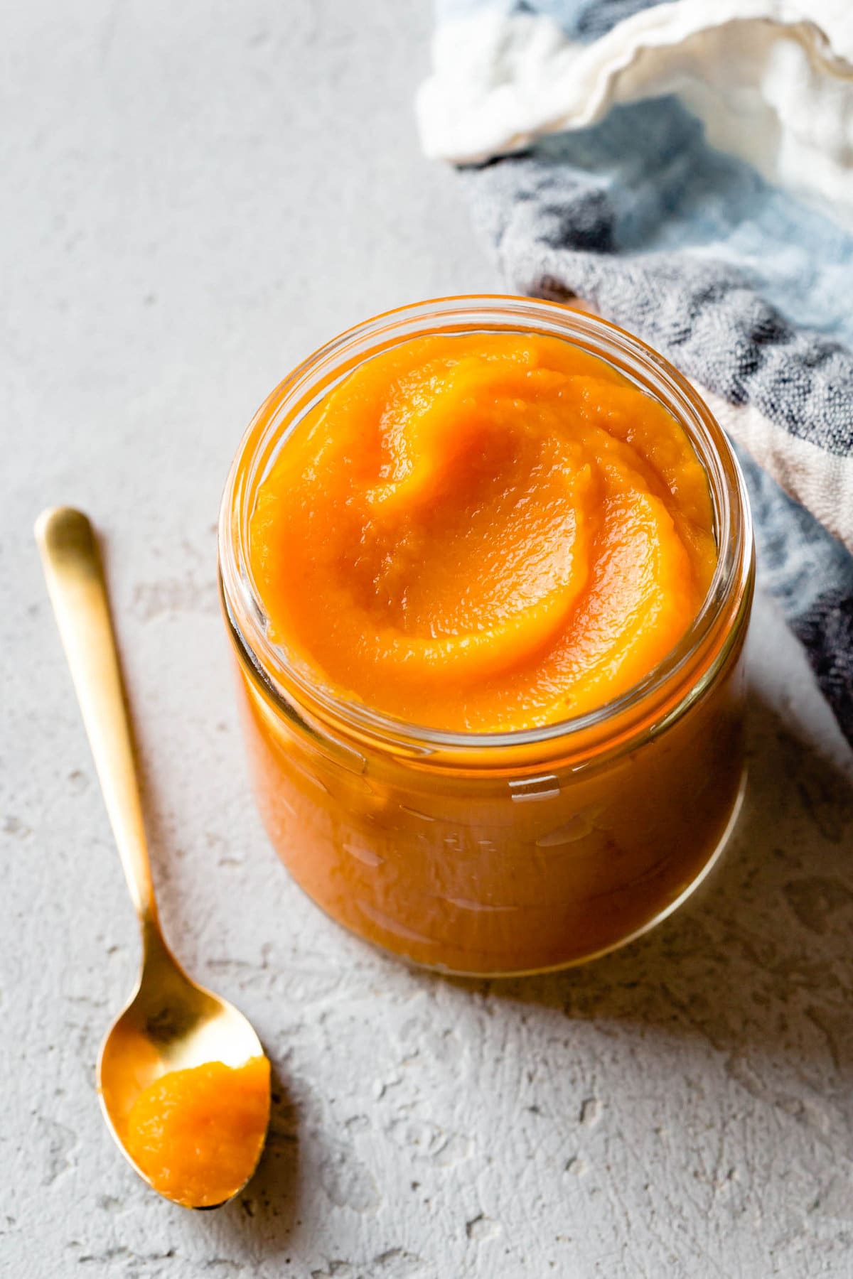 homemade "pumpkin" puree is swirled in a glass jar with a gold spoon