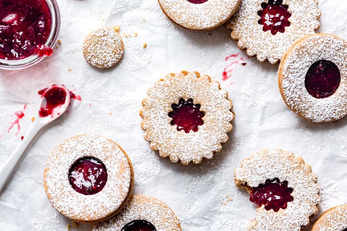 The linzer cookies have been freshly sandwiched and sit on a piece of parchment