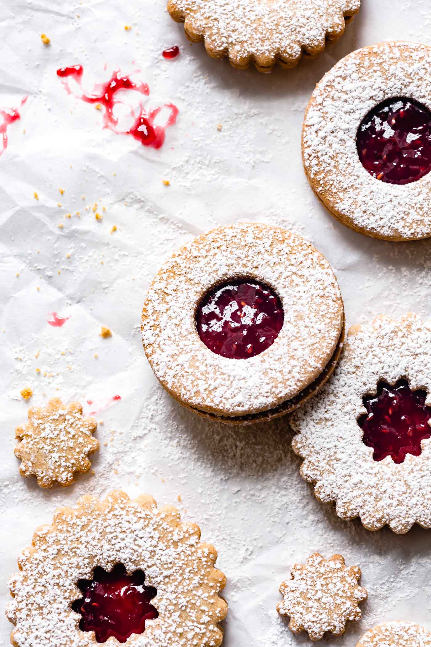 Linzer cookies sit attractively on a rumpled piece of white parchment with sprinkles of powdered sugar resembling snow all around them