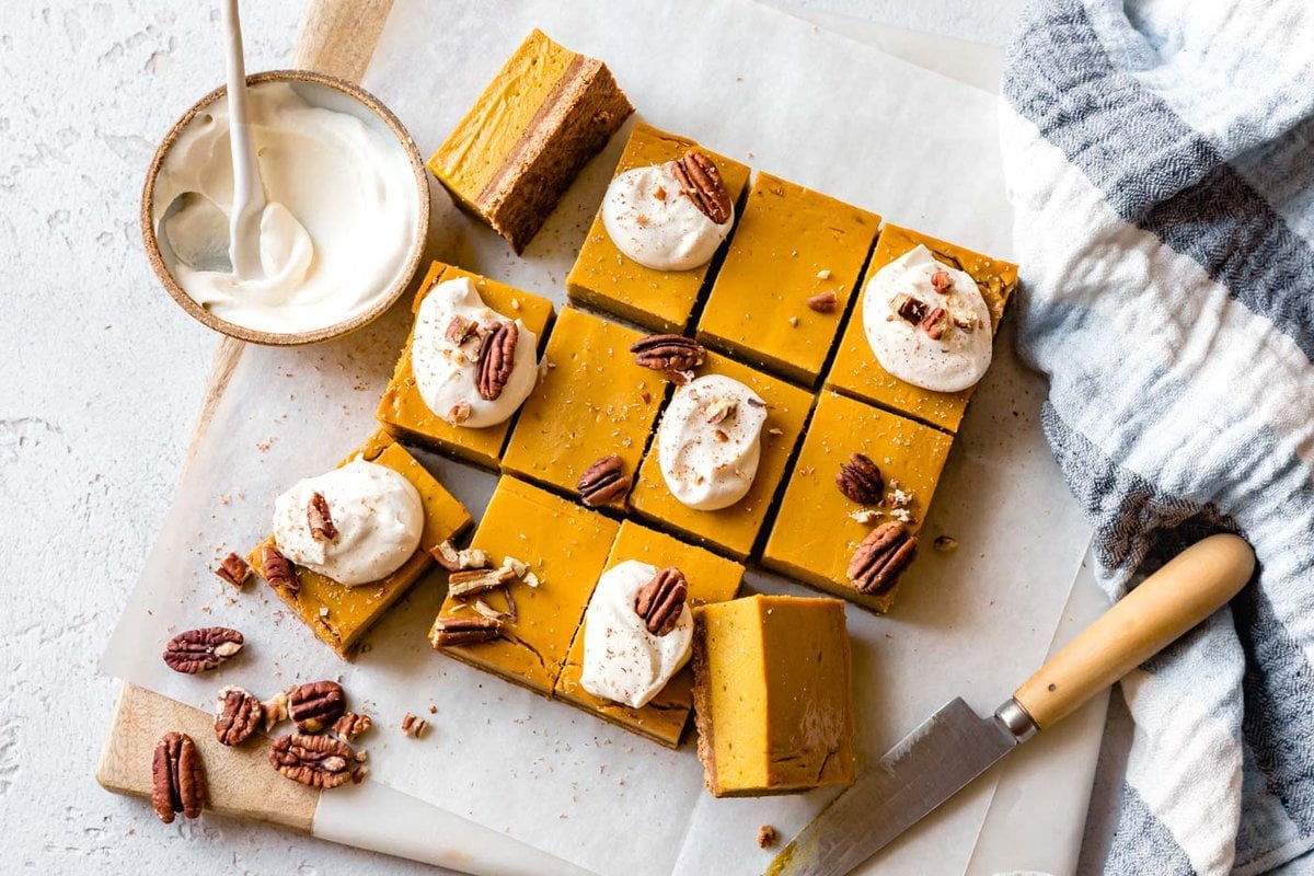 Pumpkin bars have been cut and topped with cream, nutmeg, and pecans