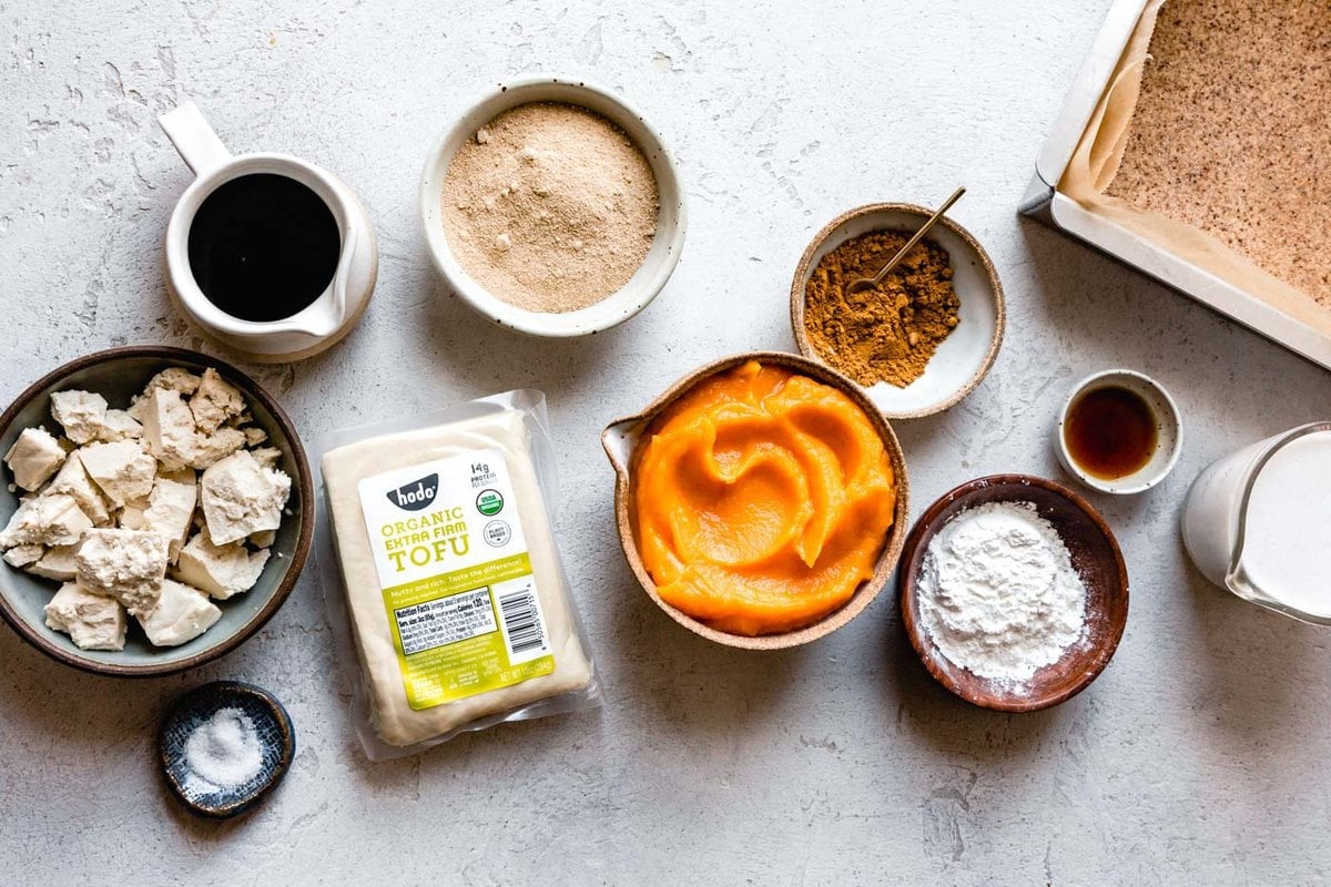 ingredients for vegan pumpkin pie bars arranged in a collection of bowls on a plaster surface