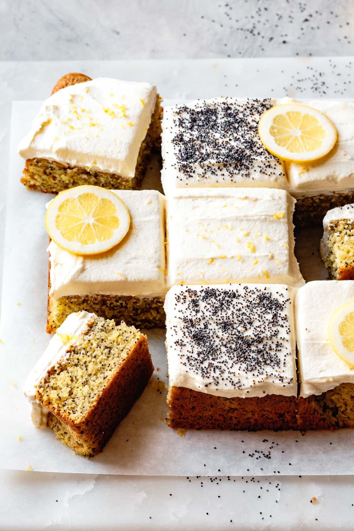 Lemon cake has been decorated with lemon wheels and poppy seeds and cut into 9 squares for the nomming.