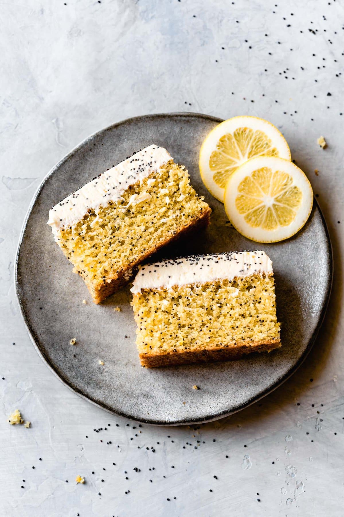 two slices of lemon cake are on a gray plate on their side showing off their sexy layers of cake and icing