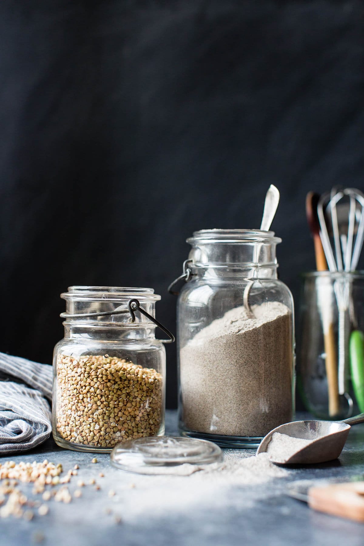 buckwheat groats and flour are in two vintage jars against a black background