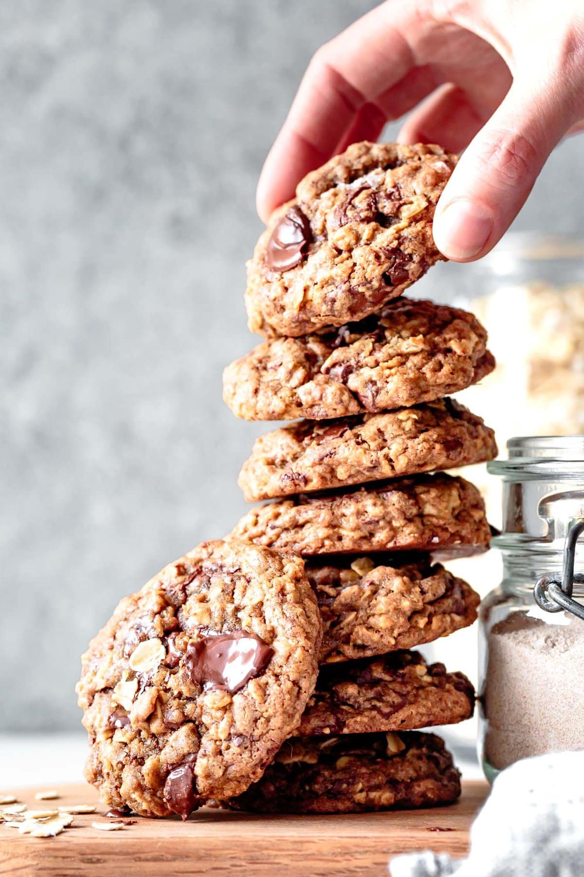 A pile of cookies shows off the face of a gooey teff chocolate chip cookie while a hand reaches for the top one