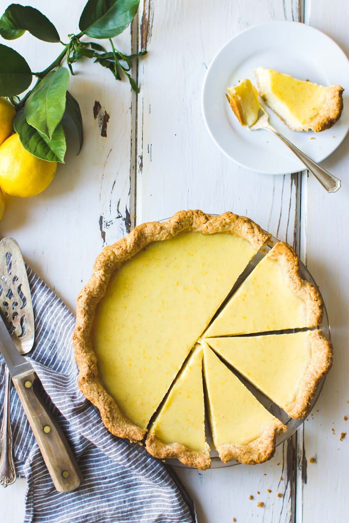 a butter-yellow pie is on a rustic white wood surface with a slice taken out