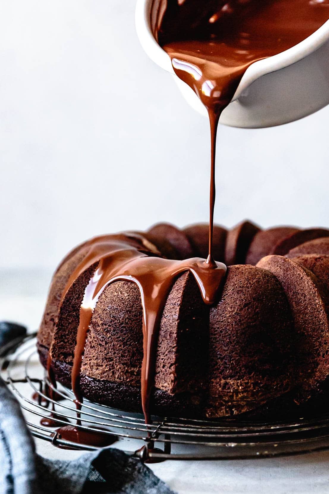 glossy creme fraiche ganache is being poured over and beautiful chocolate bundt cake