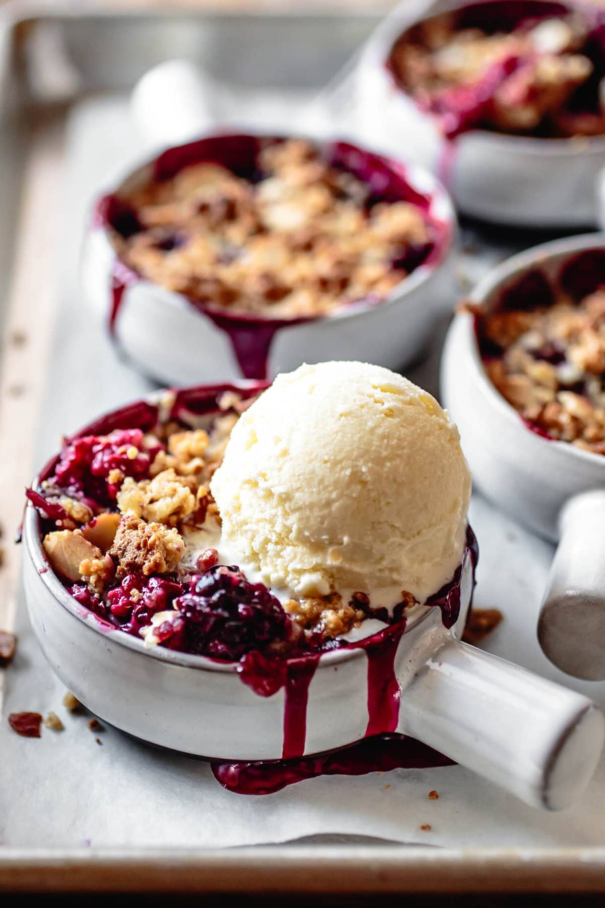 A scoop of creme fraiche ice cream melts over a pan of berry crisp
