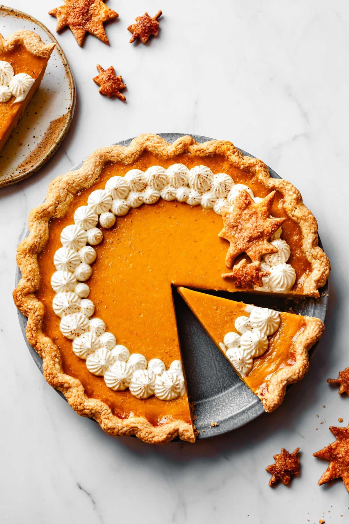 A beautiful gluten-free pumpkin pie is on a marble surface with a slice cut out and leaf cutouts on the surface
