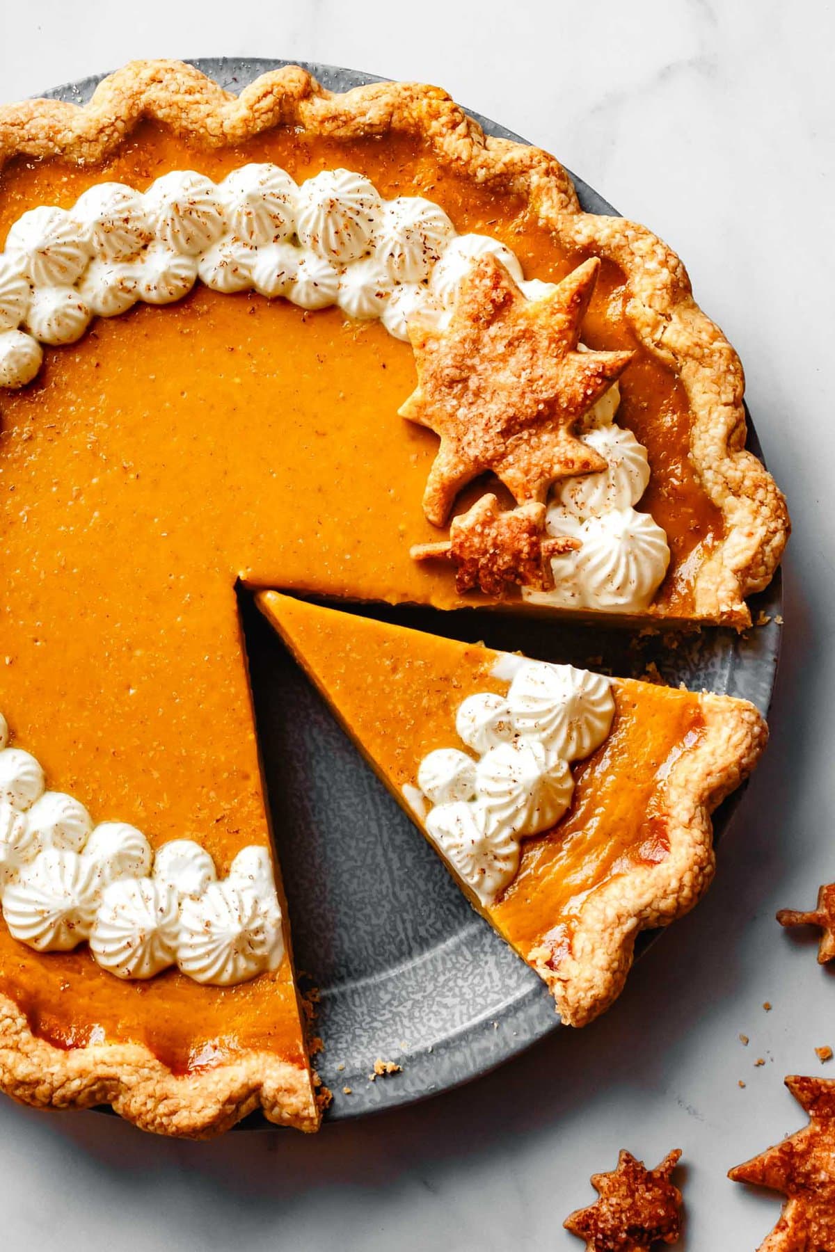 a vibrant orange gluten-free pumpkin pie has been piped with whipped topping and decorated with leaf cutouts, shown close-up