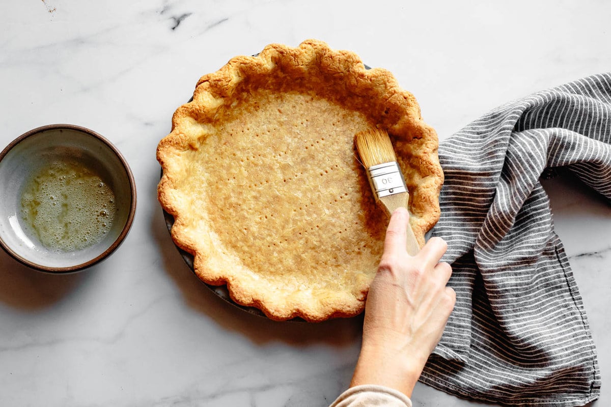 parbaked pie crust is being brushed with egg white