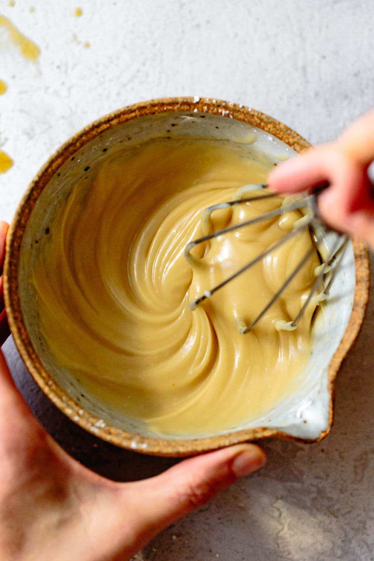hands are whisking a bowl of maple glaze