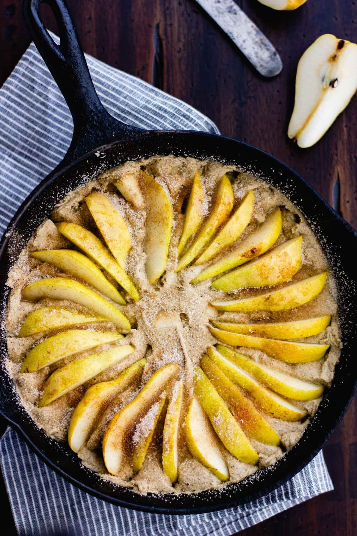 Pear wedges have been arranged on top of the cake batter in a cast iron skillet