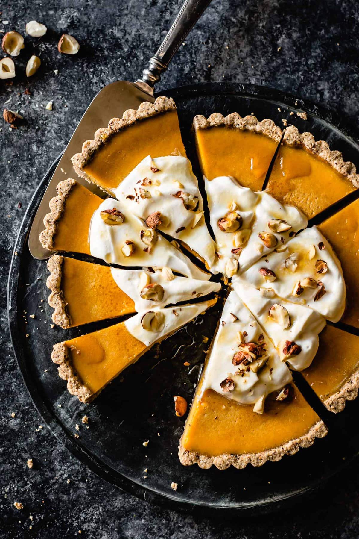 a handsome gluten-free pumpkin tart sits on a dark marble board topped with yumminess and ready to nom!