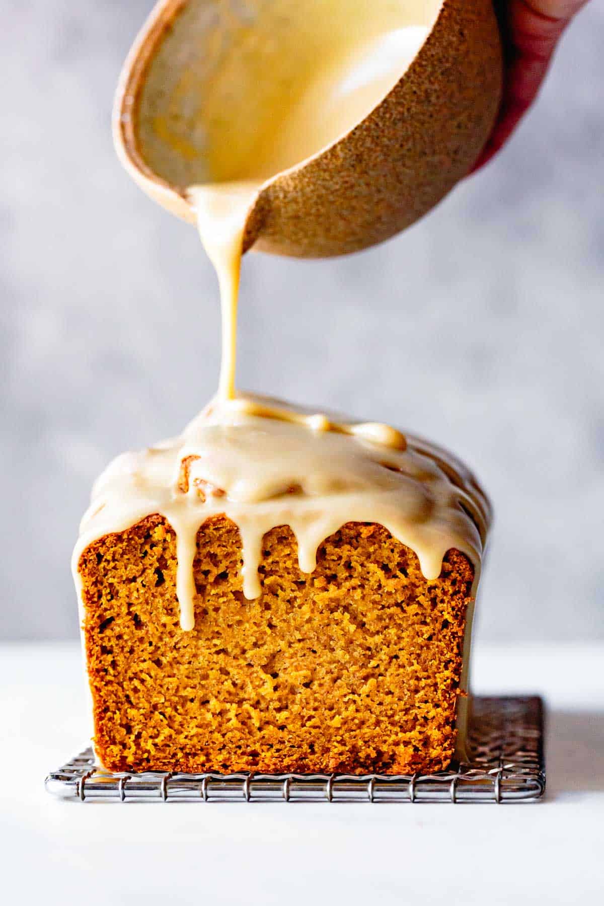 maple glaze is being drizzled over a loaf of pumpkin bread
