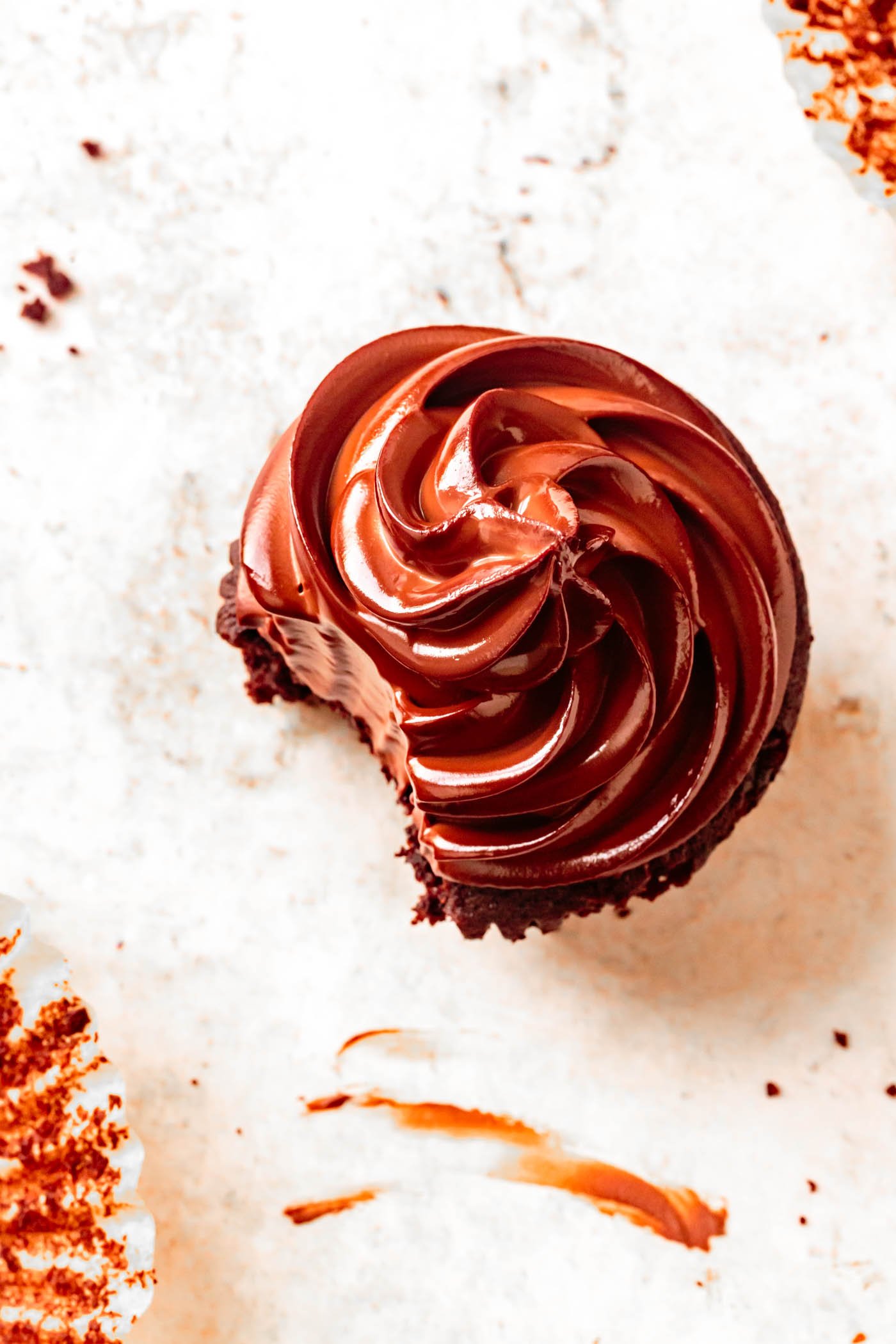 a coconut flour chocolate cupcake has a bite of glossy ganache taken out, shown overhead