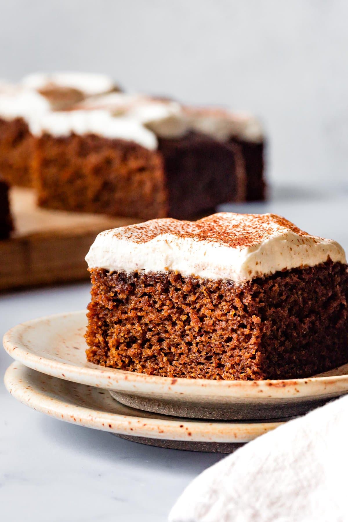 a heroic slice of gingerbread cake sits on a stack of plates showing off its floofy crumb and creamy topping