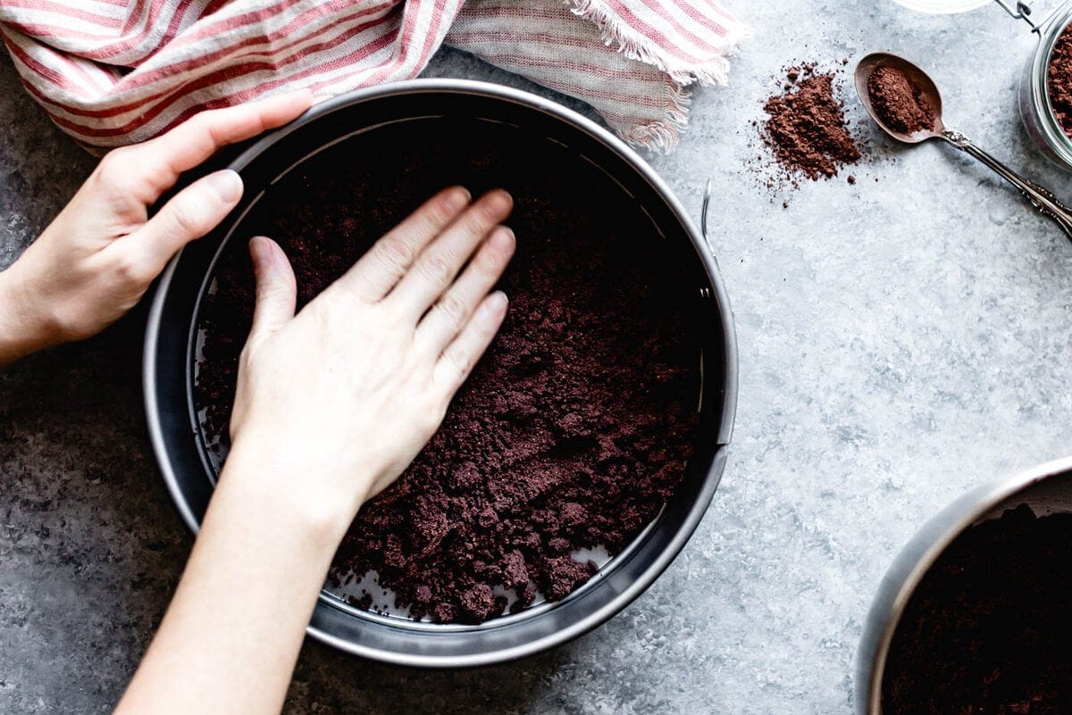 a hand presses cocoa almond flour crust into a springform pan