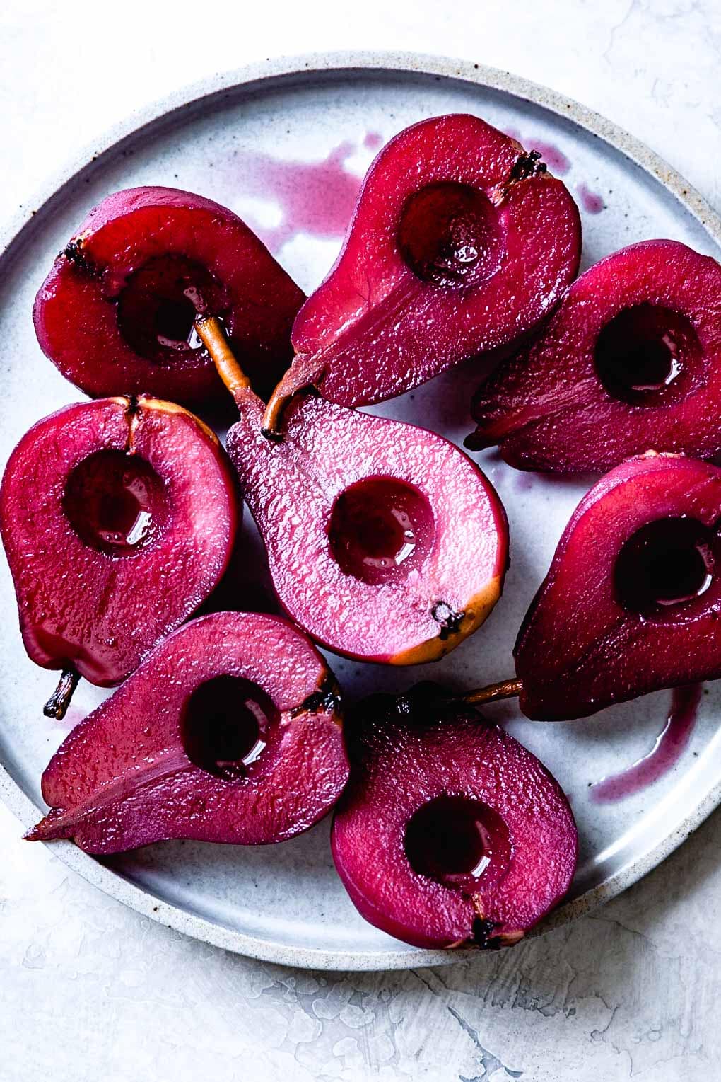 crimson poached pear halves in red wine are arranged on a blue plate