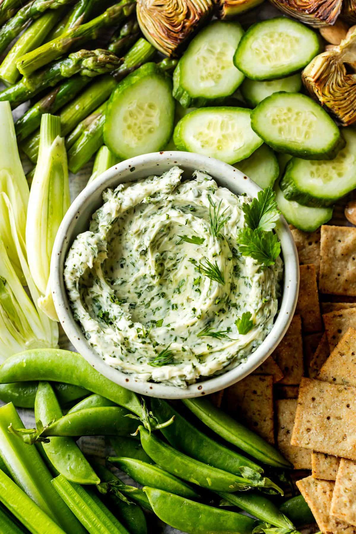 a bowl of herb butter has crudites arranged around it