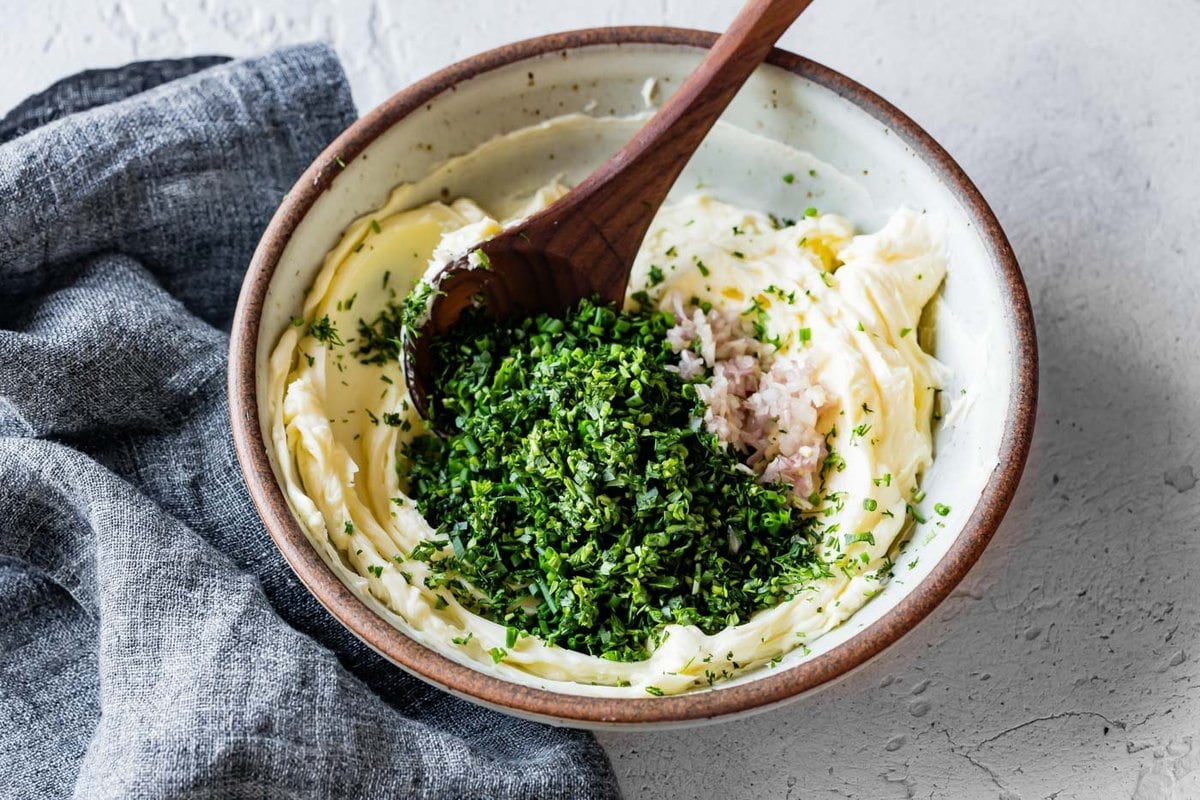butter is in a bowl with herbs and shallots