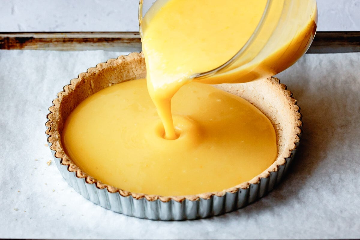 lemon curd being poured into a tart shell