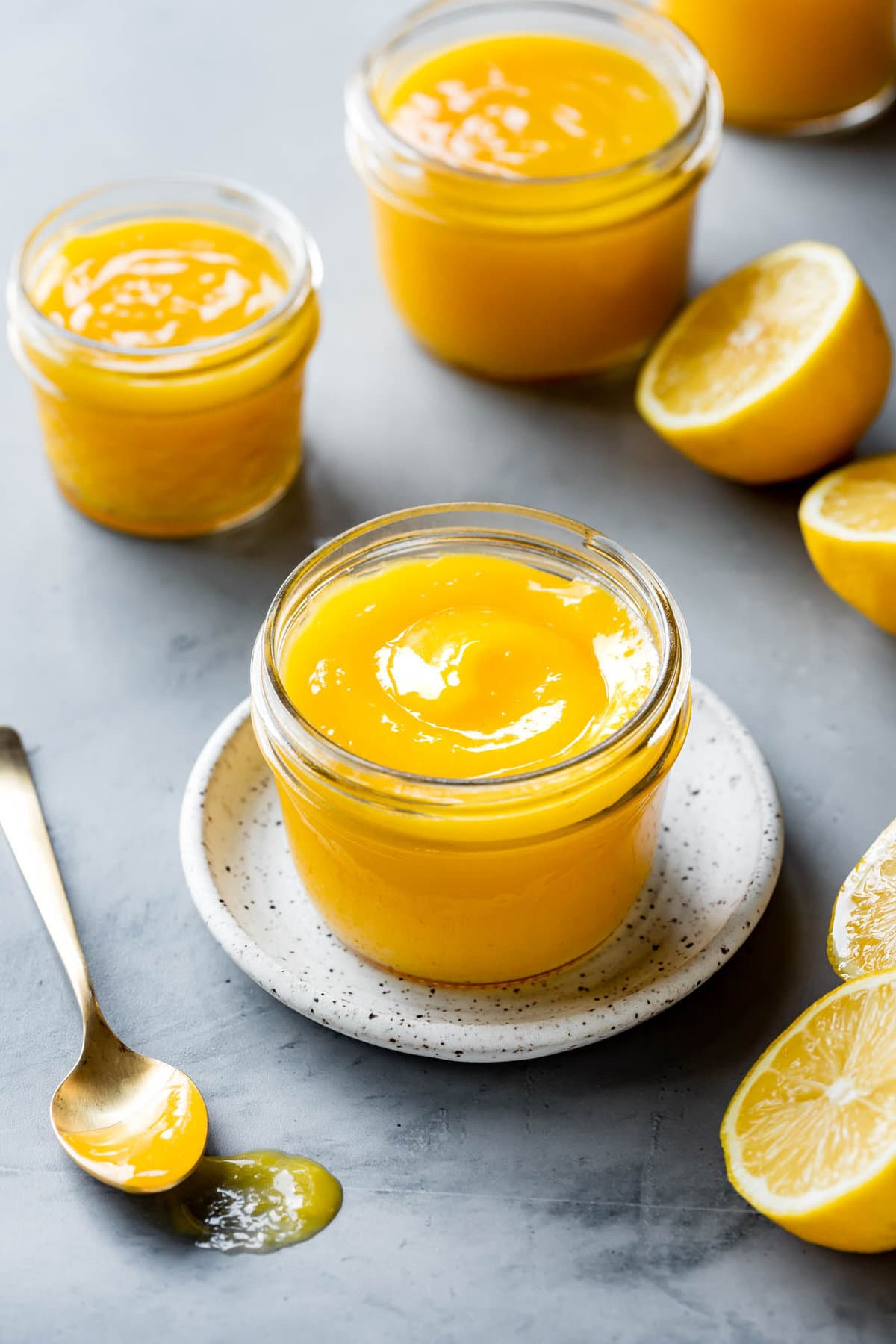 jar of lemon curd with a swirl in it on a plate with lemons around the frame