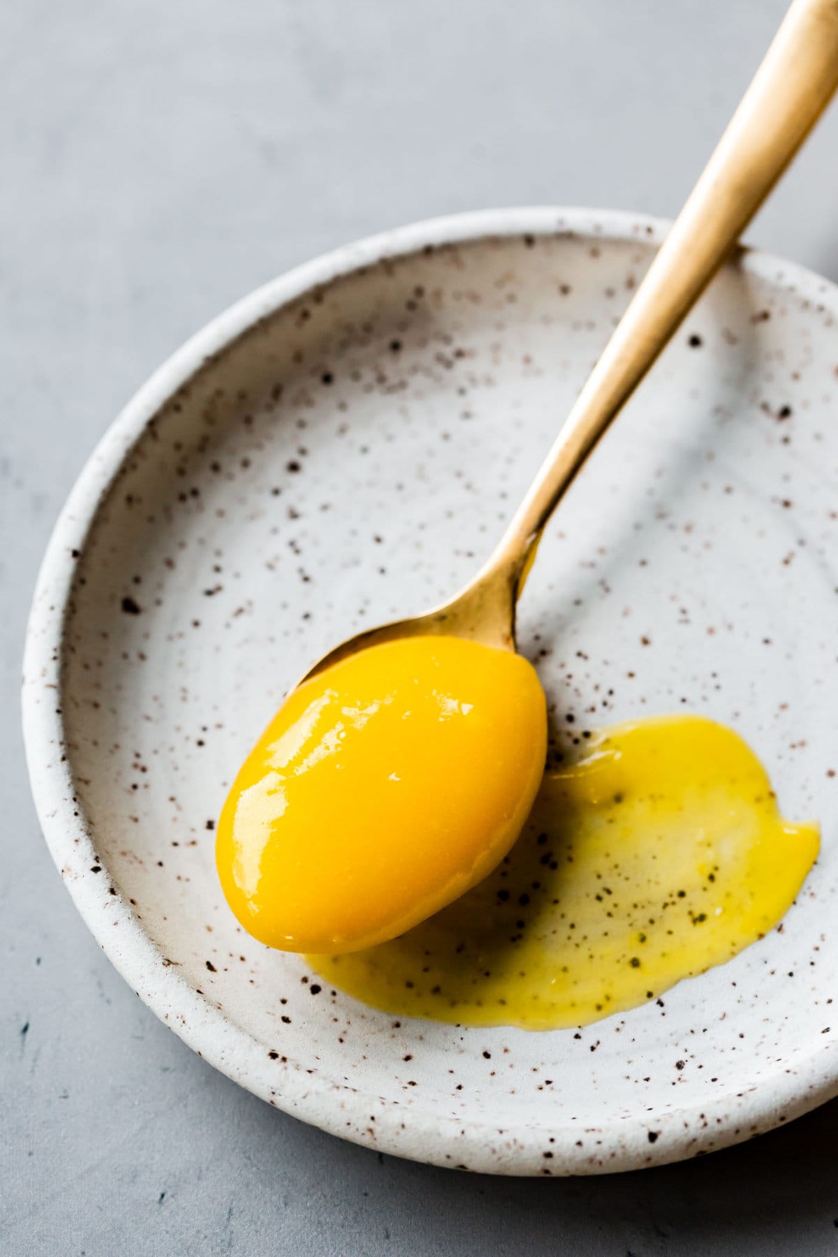 a spoonful of lemon curd sits on a plate with a smear of curd on the plate