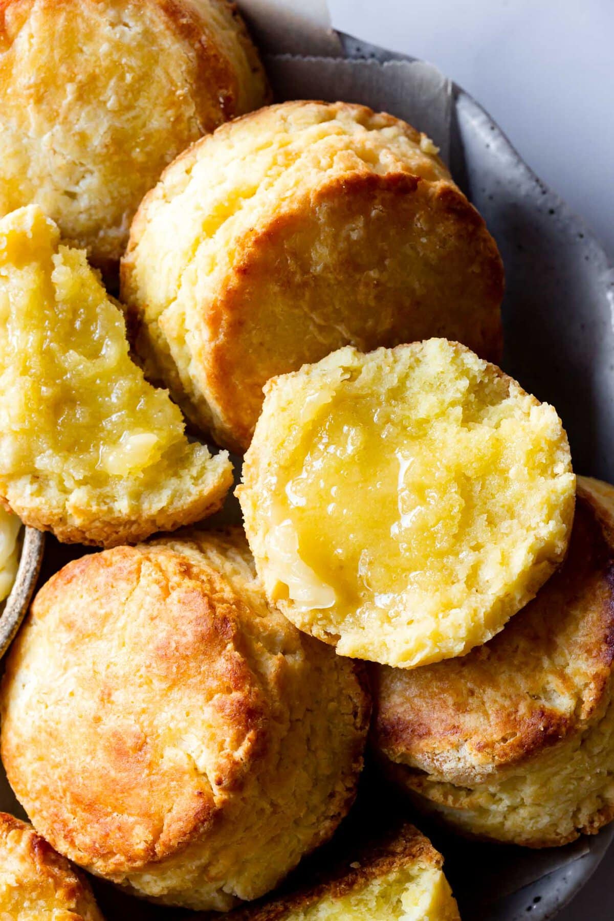 a gluten-free buttermilk biscuit has been split and topped with honey butter, showcasing its floofy insides and golden, crisp edges. 