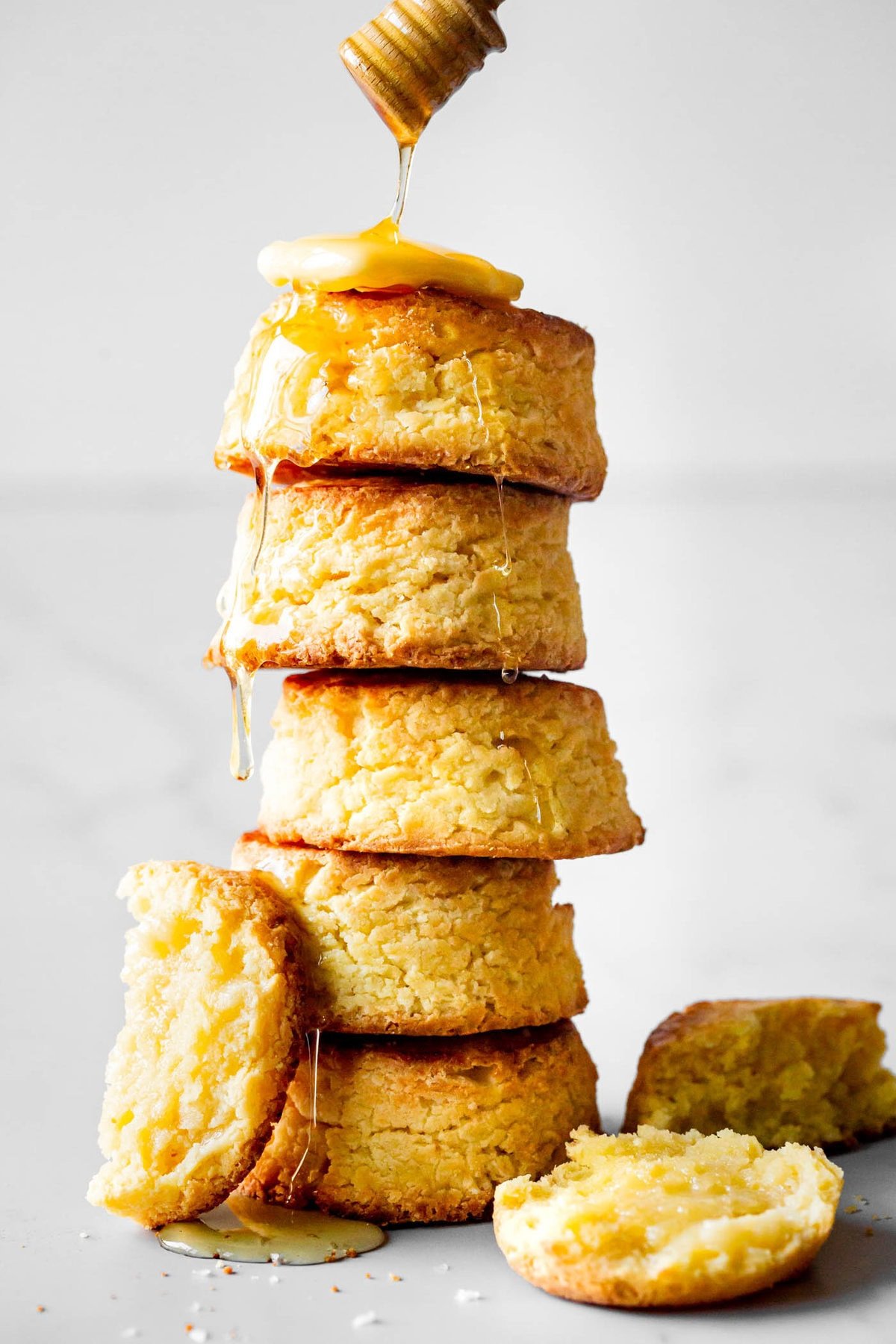 honey is being drizzled over a stack of biscuits topped with a pat of butter