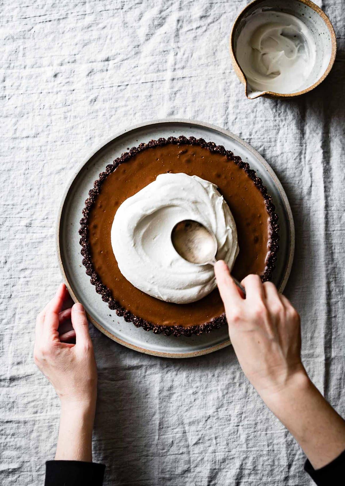 hands are swirling cream over a chocolate tart