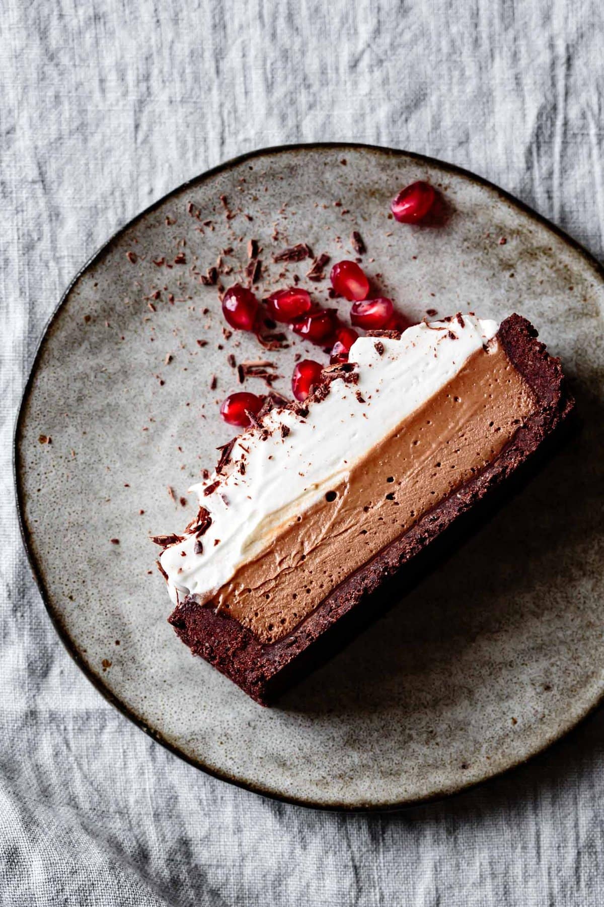 a slice of chocolate cake with whipped coconut cream and pomegranates on a plate