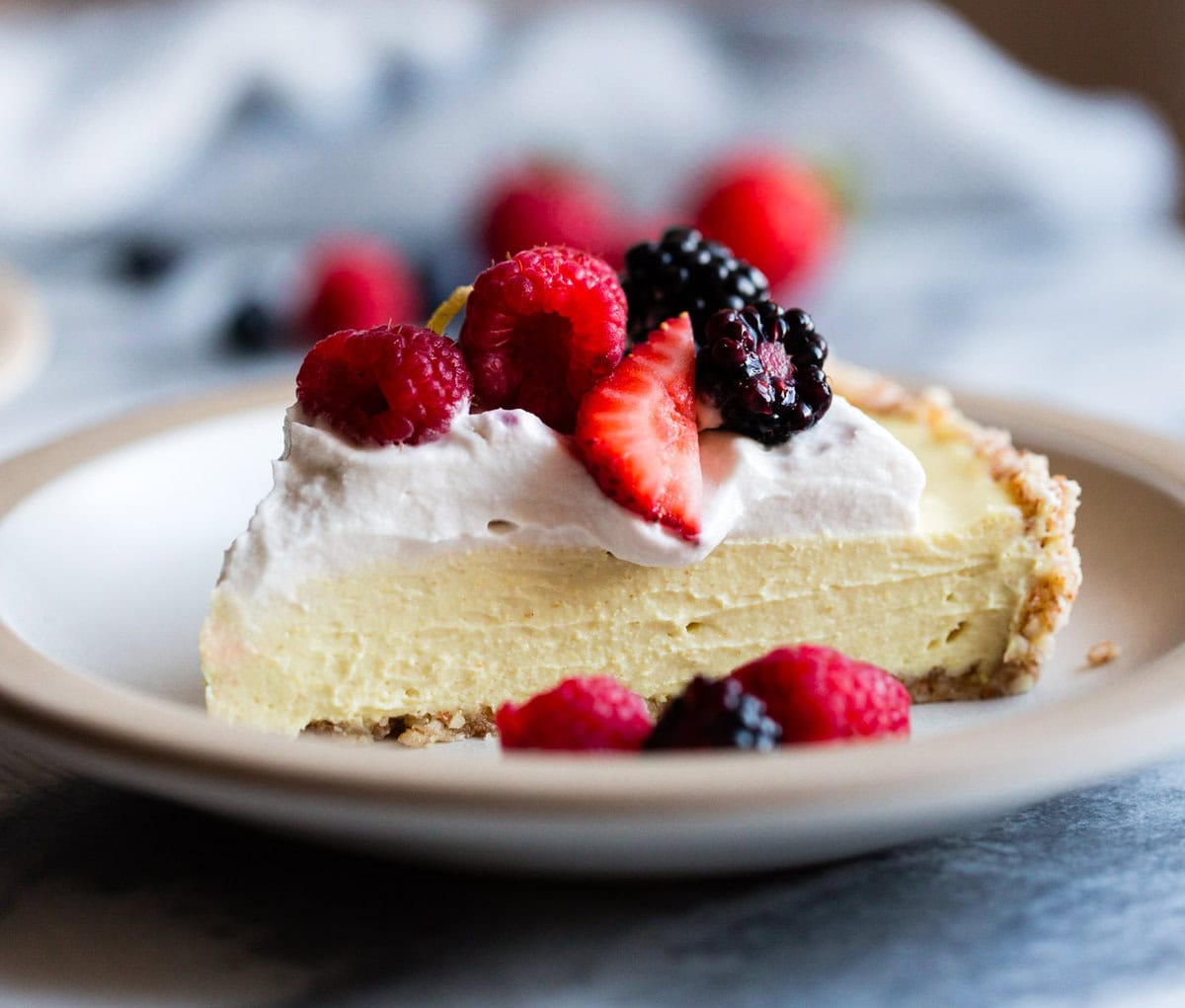 Close up slice of lemon tart topped with creamy goodness and berries