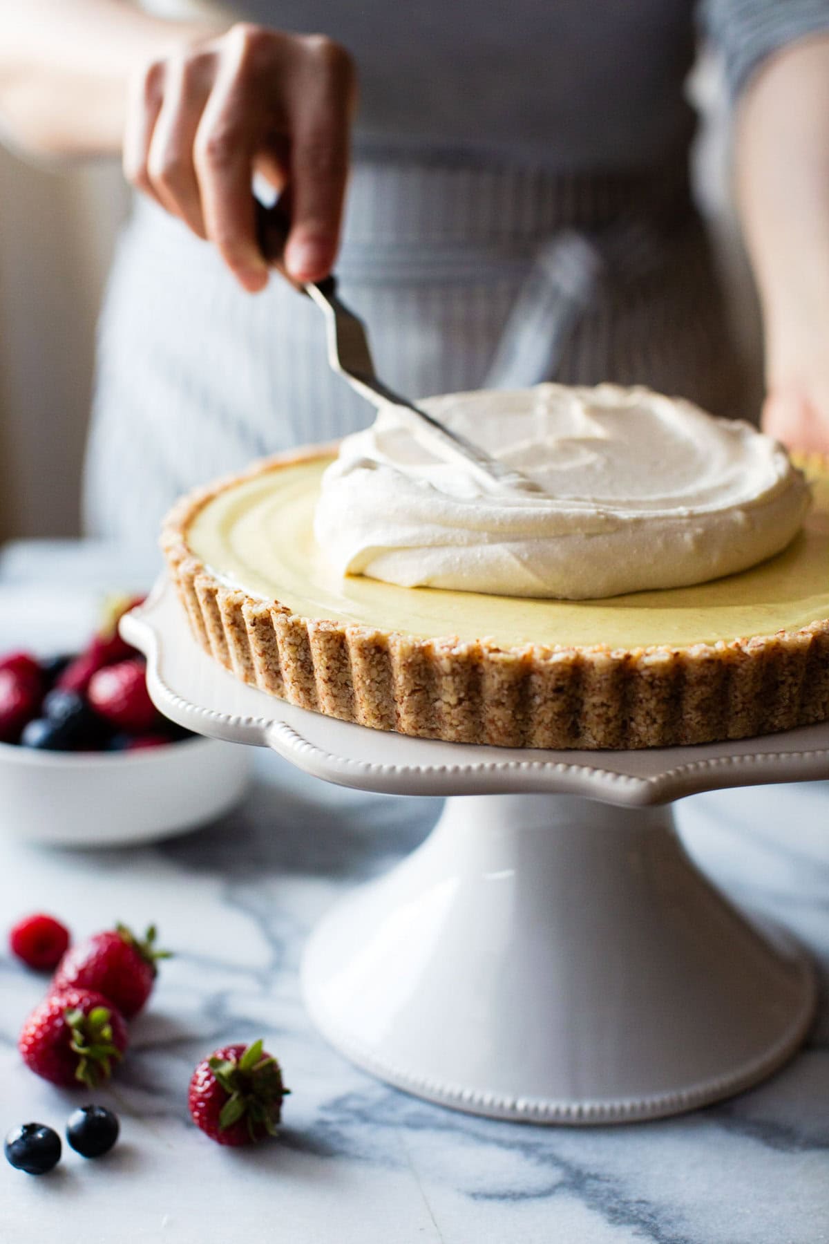 a lemon tart is on a cake stand having coconut whipped topping swirled over it