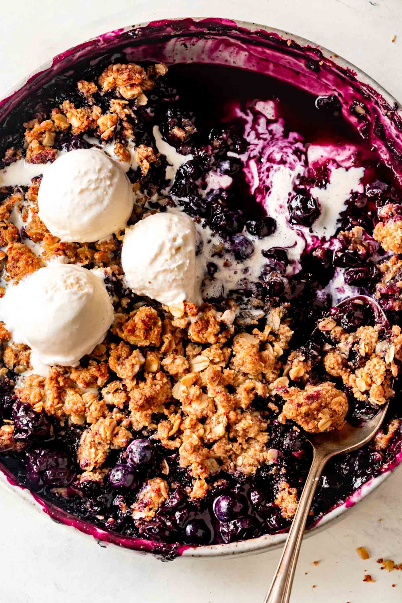 Blueberry crisp is baked in a pan and topped with melty scoops of ice cream