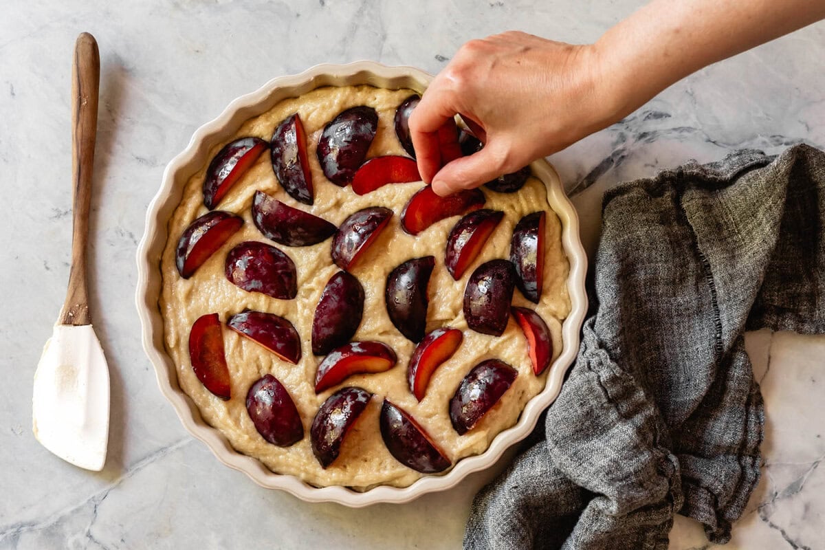 hand placing plums on the batter
